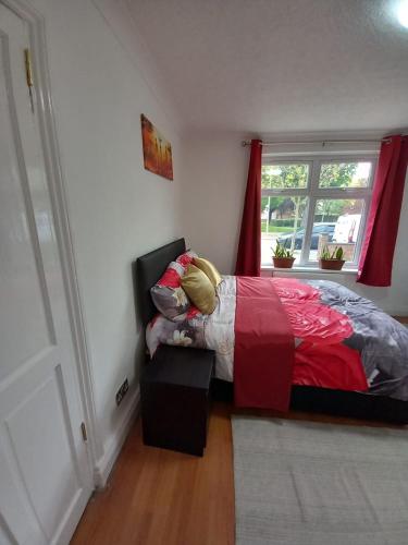 a bedroom with a bed with a red comforter and a window at JosteeStay Apartments -Rooms in Goodmayes