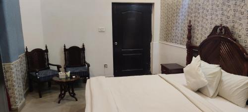 a bedroom with a bed and two chairs and a door at Hotel Shelton Palace in Multan