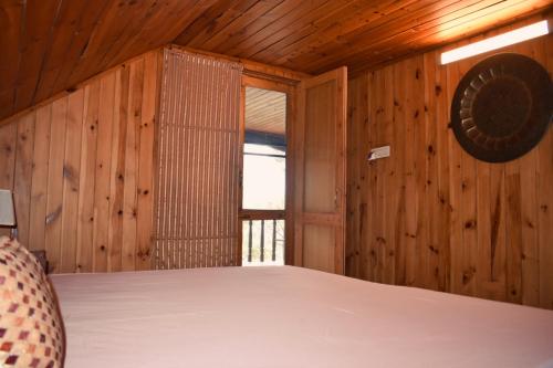 a bedroom with wooden walls and a bed with a window at The Shivdhaar Estate kud'Patnitop in Kūd