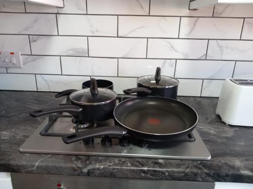 three pots and pans sitting on top of a stove at JosteeStay Apartments -Rooms in Goodmayes