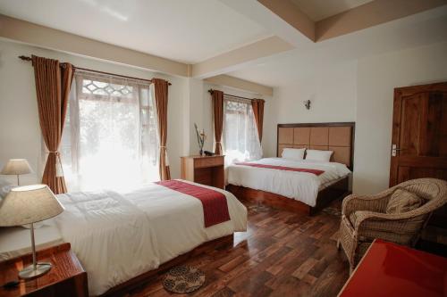 a bedroom with two beds and a chair and window at MISSION VALLEY Kalimpong in Kalimpong