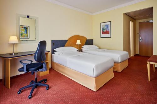 a hotel room with two beds and a desk and a chair at Sheraton Offenbach Hotel in Offenbach