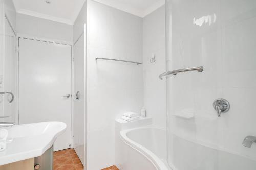 a white bathroom with a shower and a sink at Cosy Getaway with Fireplace and Spacious Backyard in Broulee