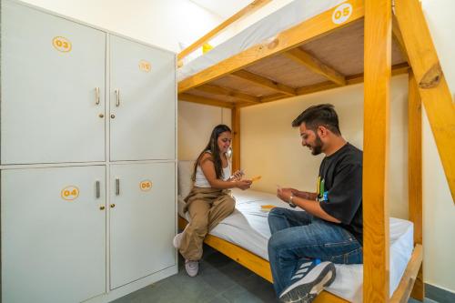 a man and woman sitting on a bed in a bunk room at The Social Stays Rishikesh formerly ArtBuzz in Rishīkesh