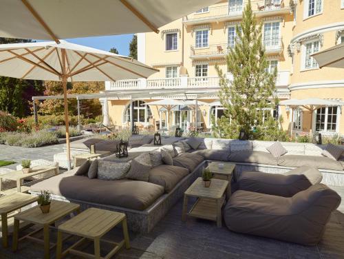 un patio con sofás, mesas y una sombrilla en Le Grand Bellevue en Gstaad