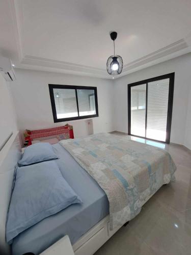 a large bed in a bedroom with two windows at Relaxing Villa with pool in El Haouaria