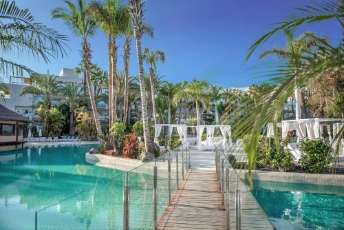 a resort pool with palm trees and a wooden walkway at Maspalomas Princess in Maspalomas