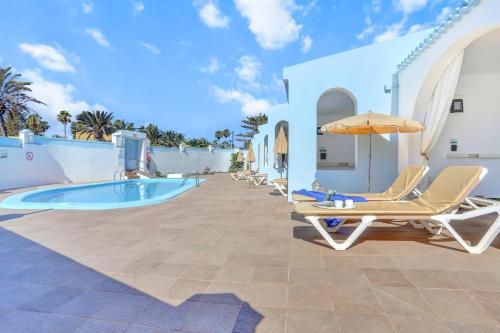 a swimming pool with lounge chairs and an umbrella at Neptuno Bungalows - Adults Only in Corralejo