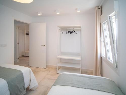 a white bedroom with two beds and a window at Sibs Sanlúcar Atlantico Playa Vistas Reformado in Sanlúcar de Barrameda