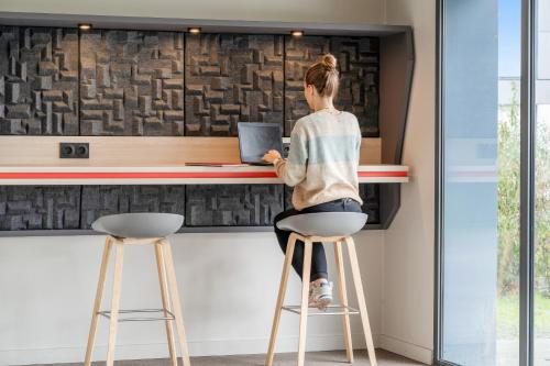 a woman sitting on a stool at a counter with a laptop at Zenitude Hôtel-Résidences Nantes Métropole in Nantes