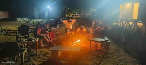 Un gruppo di persone sedute intorno al fuoco di Taste Of Hampi - Stay @ Nature a Hampi