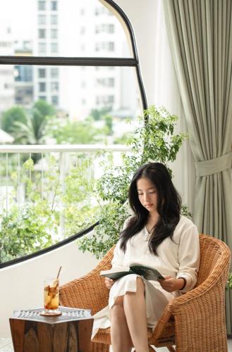 a woman sitting in a wicker chair reading a book at Saha Casa Boutique Hotel Da Nang in Da Nang