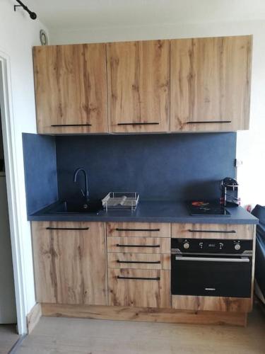 Il comprend une cuisine équipée d'une cuisinière noire et de placards en bois. dans l'établissement Studio tout confort aux Balcons de Villard de Lans, à Villard-de-Lans