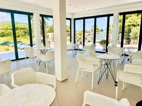 un restaurante con sillas blancas, mesas y ventanas en Hotel Vila Park Bujari, en Ksamil