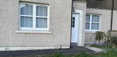 una casa con dos ventanas y una puerta blanca en Two bedroom ground floor apartment with garden, en Falkirk