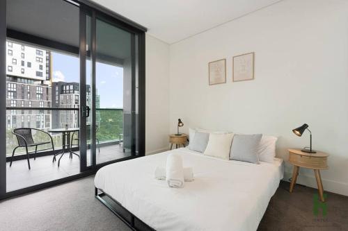 a bedroom with a large white bed and a balcony at Cozy 1 bedroom at Olympic Park with one carspace in Sydney