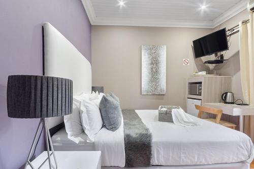 um quarto com uma cama, uma mesa e uma televisão em Botle Ba Afrika Lodge em Vereeniging