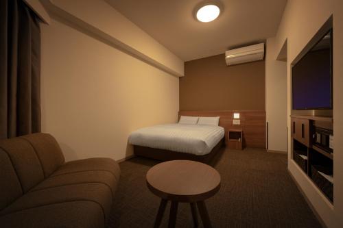a hotel room with a bed and a couch and a tv at Dormy Inn Morioka in Morioka