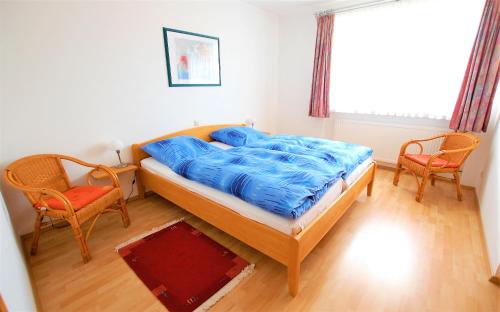 a bedroom with a bed with blue sheets and two chairs at Gästehaus Jäger Ferienwohnungen in Gersfeld