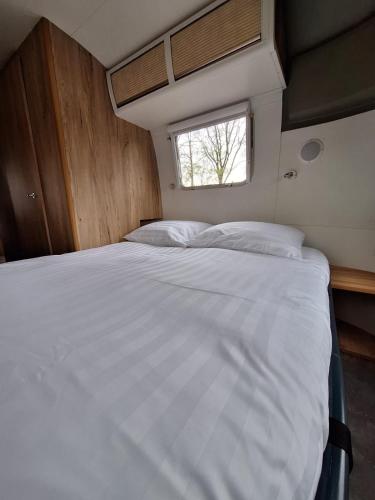 a large white bed in a room with a window at Amerikaanse Airstream caravan met hottub in Kessel