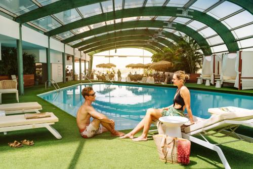 Ein Mann und eine Frau sitzen neben einem Pool in der Unterkunft Arrecife Gran Hotel & Spa in Arrecife