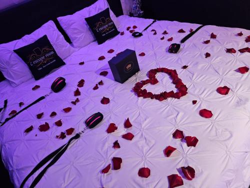 a bed covered in red rose petals on a white sheet at "l'Escape room" - love room atypique in Saint-Martin-des-Entrées