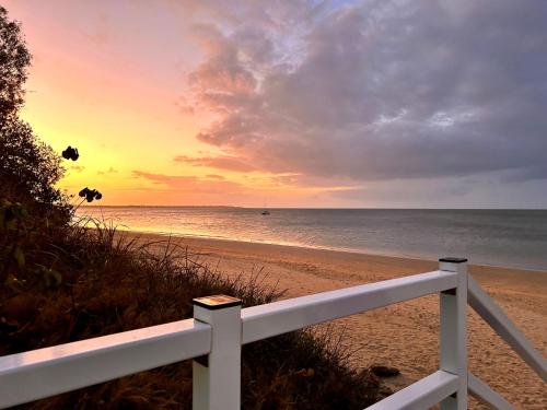 a sunset on a beach with a white fence at Vila Paus Dua - Beachfront Hervey Bay in Hervey Bay