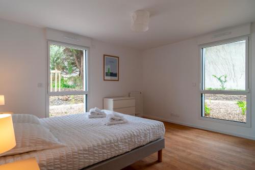 une chambre blanche avec un lit et deux fenêtres dans l'établissement Trévarec au Cabellou - Appartement jardin sur la plage, à Concarneau