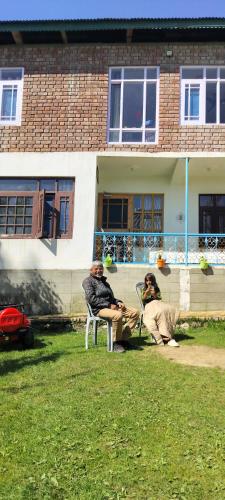 two people sitting in chairs in front of a house at Elizabeth paying guest house Tangmarg gulmarg in Gulmarg