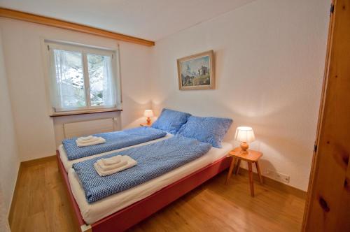 a bedroom with a bed with blue sheets and a window at Haus Bodmen C, Apartment Grünsee in Zermatt