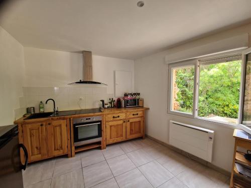 une cuisine avec des armoires en bois, un évier et une fenêtre dans l'établissement Duplex avec jardin et grande terrasse 8 personnes, à Campagnan