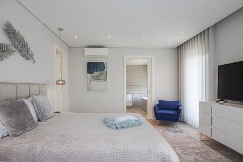 - une chambre avec un lit, une télévision et une chaise bleue dans l'établissement Villa Moroz - BY BEDZY, à Almancil