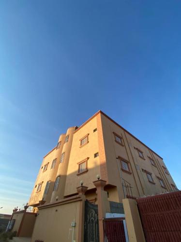 een hoog gebouw met een blauwe lucht op de achtergrond bij شقق الزهور in Al Wadeen