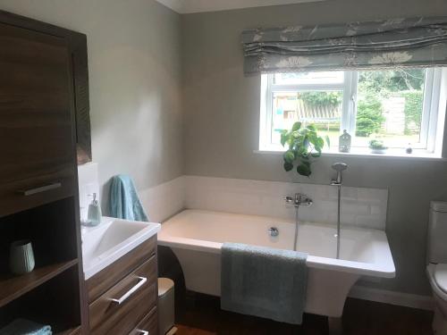 ein Bad mit einer Badewanne, einem Waschbecken und einem Fenster in der Unterkunft En-suite with double bed on mezzanine and desk in family home in Hertford