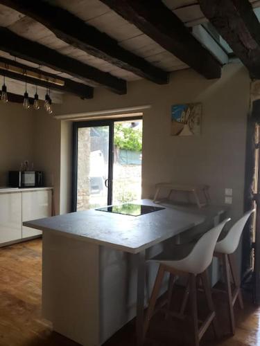 une cuisine avec une grande île et 2 chaises blanches dans l'établissement Maison du mur jaune, à Tourtoirac