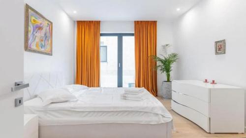 a white bedroom with a large bed and orange curtains at Turegatan Top Class Apartment in Stockholm