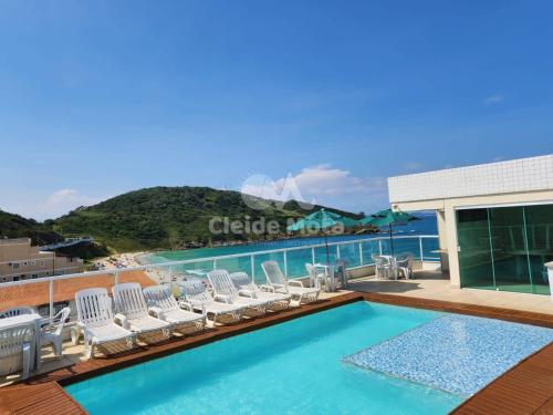 Una piscina con tumbonas y el océano. en Vista Maravilhosa, 3 Quartos, Lazer com Piscina, Churrasqueira e 2 Vagas, en Arraial do Cabo