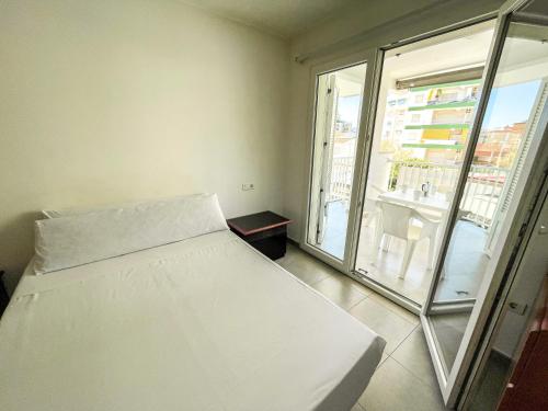 Cama blanca en habitación con ventana grande en Apartamentos Gandía Centro 3000, en Gandía