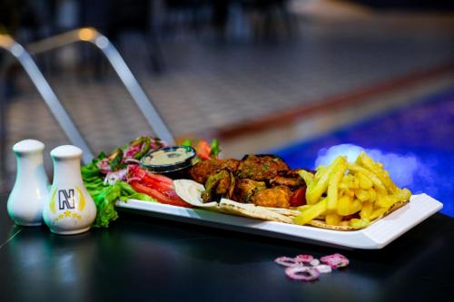 a plate of food on a table with french fries at Nesto Hotel in Manāwirah