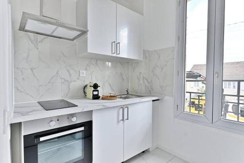 a white kitchen with white cabinets and a window at Appartement Rose Moderne Proche de la capitale in Gagny