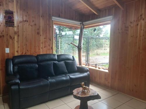 a black leather couch in a room with a window at Cabaña Beatriz in Coñaripe