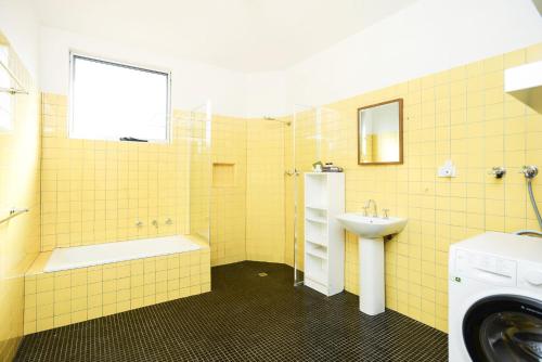 y baño de azulejos amarillos con lavabo y lavadora. en Pelican Cottage - Pet Friendly - Wifi en Goolwa North