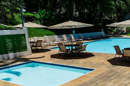 a swimming pool with chairs and tables and umbrellas at Mara Palace Hotel in Vassouras