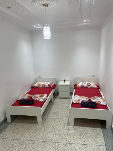 two beds in a room with red and white sheets at Résidence Bario H in Al Hoceïma