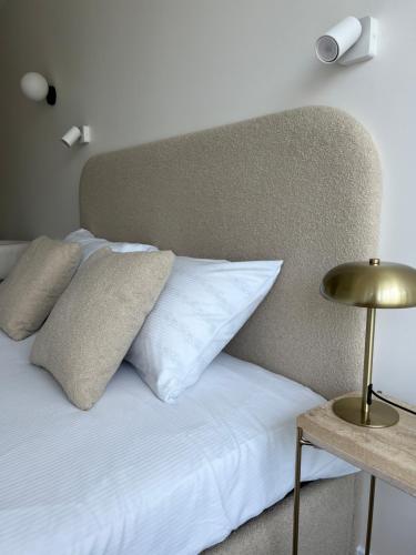 a bed with white sheets and pillows and a lamp at Apartamentai-studija Palangos kopos in Palanga
