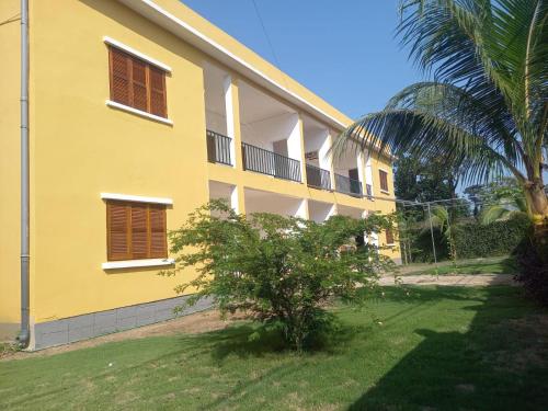 a yellow building with a palm tree in front of it at Moradia Turística MJ ROOMS CITY in São Tomé