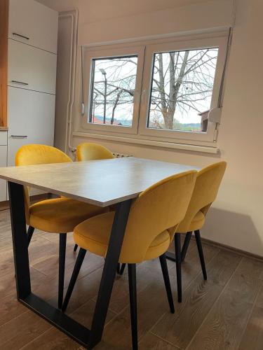 a dining room table with yellow chairs and a window at Apartman Sutla in Kumrovec