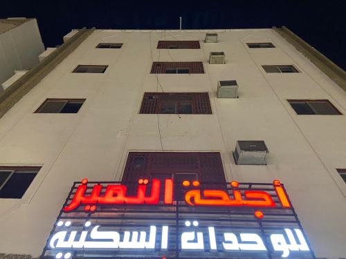 a tall white building with a neon sign on it at اجنحة التميز للوحدات السكنية in Medina