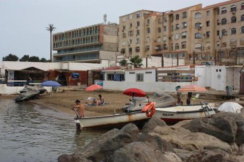 grupa ludzi siedzących na plaży z łodziami w obiekcie Résidence hadji w mieście Sidi Ferruch