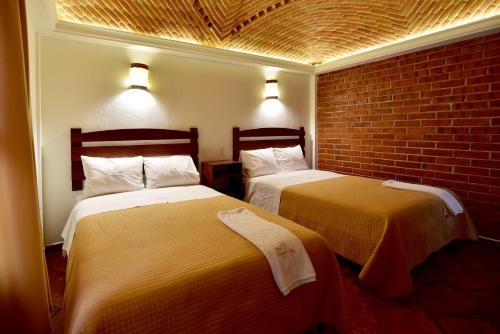 two beds in a room with a brick wall at Hotel Santa Irene in Cholula